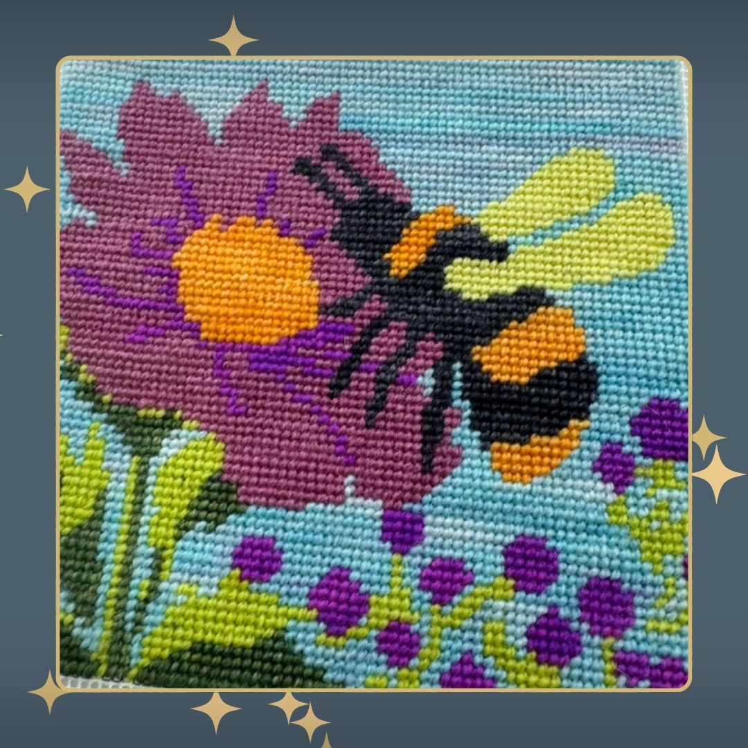 Stitched needlepoint canvas featuring a large flower and bee, with colorful wool threads.