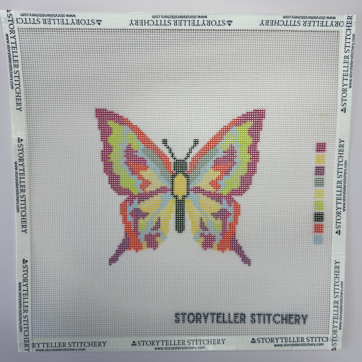 Storyteller Stitchery printed cotton needlepoint mono canvas (14 count) featuring a colorful butterfly design with pink, yellow, lavender, and mint green wings, black body, and a pale blue background. Color key printed along the right edge.