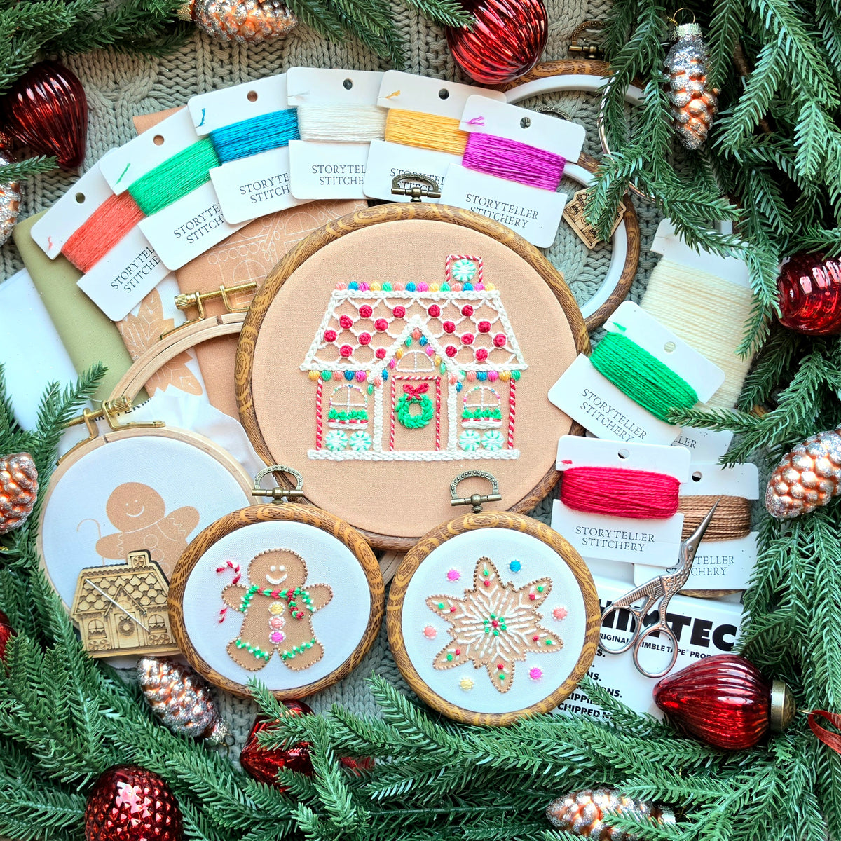 Gingerbread embroidery collection featuring stitched house, man, and star hoops, matching thread cards, and accessories displayed in a festive pine wreath with ornaments.