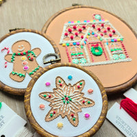 Gingerbread-themed embroidery designs featuring a stitched house, gingerbread man, and star cookie in wooden hoops.